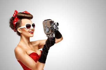 Retro movie style / Retro photo of a pin-up girl with an old vintage 8 mm camera on grey background.