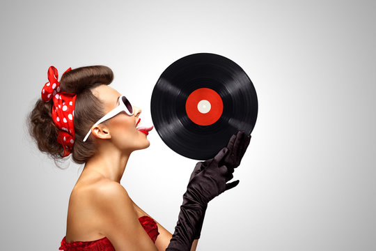 Taste and listen / Beautiful pinup bikini model, licking LP microgroove vinyl record on grey background.