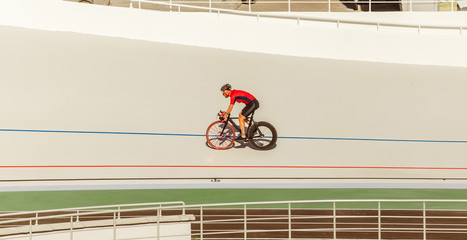 Bicyclist on cycle track outdoor. Active man racing at white velodrome.