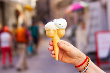 Woman holding an ice cream in a waffle cone on a busy city street  background.