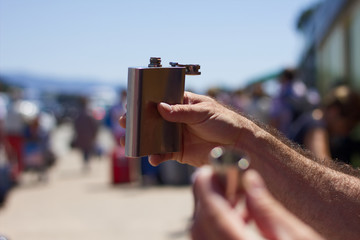Toast of a hip flask on a successful journey.  A metal plated bottle in a male hand who drinks alcohol before departure. 