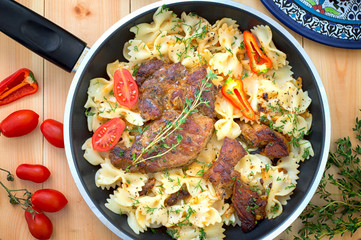 Farfalle pasta with roast meat, tomatoes close-up on a pan. Vertical view from above. Close-up
