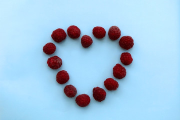 Raspberries organized in the shape of heart. Light blue background.