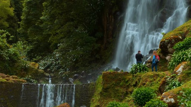 Exploring the Azores - Two tourists photographing a waterfall in the Parque Natural Ribeira dos Caldeiroes in Sao Miguel, Portugal. The Azores are one of the hidden gem destinations in Europe.