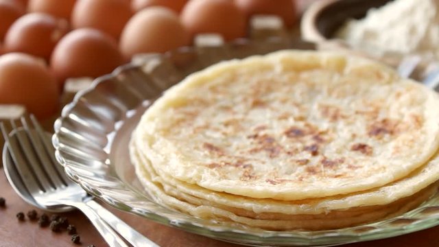 Warm roti paratha is placed onto a plate in a kitchen filled with natural light
