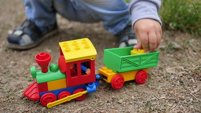 A child plays with a toy train on the sand. Outdoor games