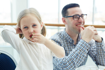 Hungry child eating strawberry with her father on background