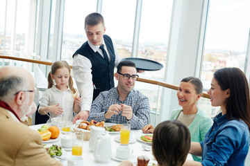 Fototapeta premium Young waiter serving big family during dinner or breakfast