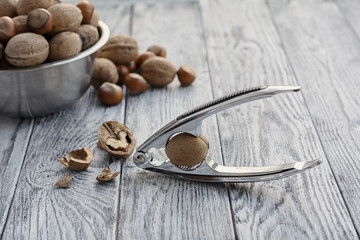 metal bowl with nuts and nutcracker on grey wooden background