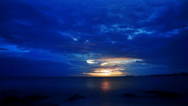 Dramatic blue and yellow sunrise over the ocean with clouds, highlighted from the down by the rising sun. Timelapse FullHD 1080p.