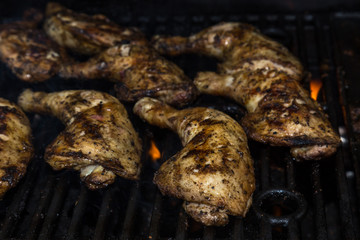 Chicken leg quarter thighs on a barbecue grill, golden and crispy with spots of fire -  side view