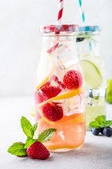 Two glass bottles with lemonade from fresh citrus lemon, raspberries, blueberries, lime and mint with drinking straws. Healthy summer beverage. Copy space, selective focus.