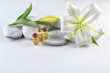 Spa stones, beautiful lily and bottles with aroma oil on white wooden background