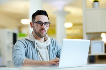 Pensive businessman sitting by workplace and typing