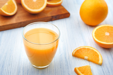 Glass of fresh orange juice and fruit slices on white wooden background