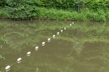 Brown water river crossed by white buoys and net © LuXpics