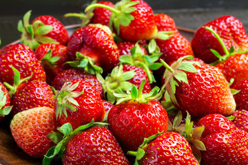 Fresh organic strawberries in plate on dark wooden planks background