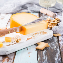 Delicious dutch gouda cheese with cheese blocks, crackers, walnuts and special knife on oud wooden table. Copy space.