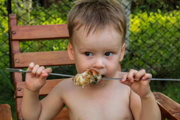 Tubby boy with pleasure eats a shish kebab. Camping. Healthy nutrition and diet. summer picnic.