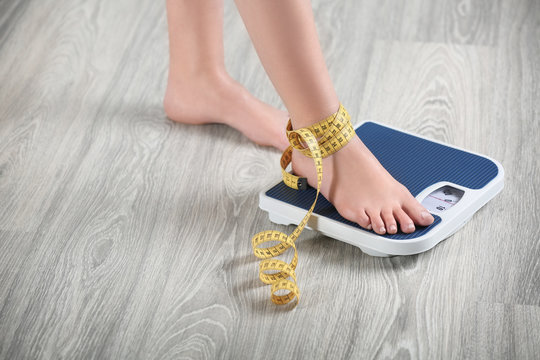 Woman standing on scales with measuring tape on wooden floor. Concept of weight loss