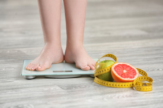 Woman standing on scales near fruits and measuring tape on wooden floor. Concept of weight loss