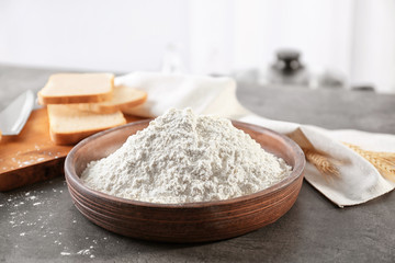 Fototapeta na wymiar Bowl of wheat flour on blurred background