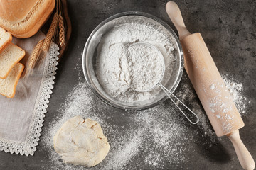 Sieve and bowl of flour on dark table, top view