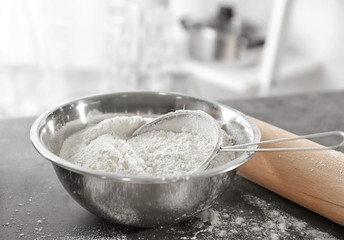 Sieve and bowl with flour on blurred background, close up
