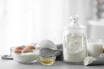 Jar and scoop of flour with ingredients for dough on blurred background