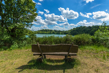 Wood made rustic bench facing a wonderful view with green water lake and blue sky with white clouds