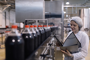 Young happy female worker in bottling factory writing notes about bottles before shipment....