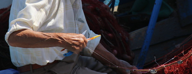 mani di un pescatore al lavoro sulle reti 