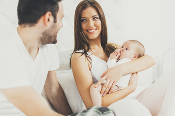 Happy family with newborn baby on the bed in room