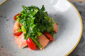 Close-up salad of red fish, arugula, cherry tomatoes, sesame, spices, beautiful trendy dish, restaurant, bright, tasty, colorful