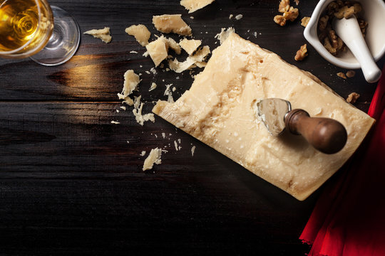 Slice of parmesan cheese with knife, nuts and wine over a wooden table