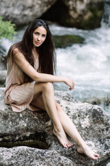 Beautiful brunette sitting on a rock in the middle of the river, water, waterfall. Beautiful nature, natural light, soft, filling