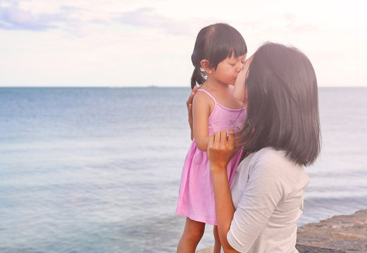 Happy family, mother and kid girl kissing with natural emotion smiling on sea background in the evening.
