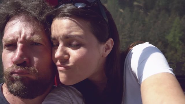 Happy couple in cableway in mountains making selfie kissing doing faces