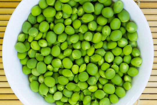 A plate of fresh green peas on a bamboo table