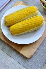 Two corn cobs are in a white dish on wooden butcher
