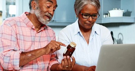 African American senior couple holding medicine bottle and using laptop - Powered by Adobe