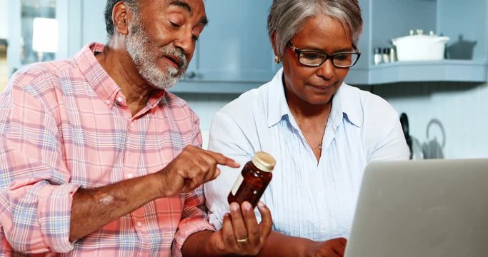 African American senior couple holding medicine bottle and using laptop