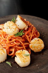 Pasta with fried scallops and tomato sauce on black wooden plate