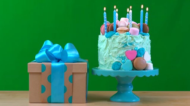 4k Green screen with blue showstopper cake decorated with marshmallows, candy and macaron cookies, and beautifully wrapped gift, candles burning.
