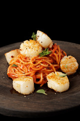 Pasta with fried scallops, oragano and tomato sauce on black wooden plate