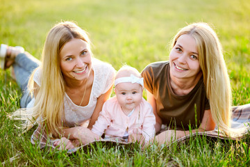 Two young mothers are walking in the park in summer with her baby. LGBT Lesbian Couple. The concept...