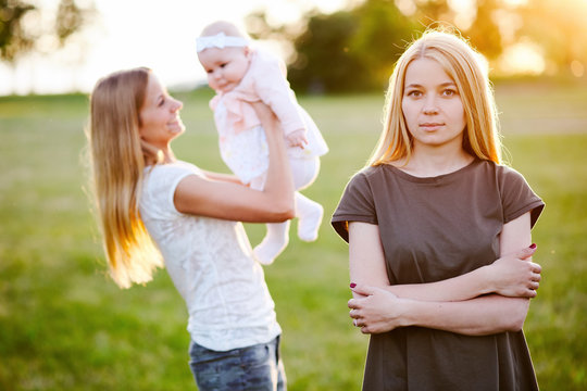 Two Young Mothers Are Walking In The Park In Summer With Her Baby. LGBT Lesbian Couple. The Concept Of  Family And Healthy Lifestyle