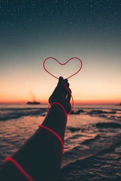 Simbolo del cuore tenuto in mano di fronte al tramonto nel mare.