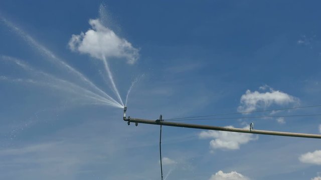 Irrigation system sprinkler for water supply over blue sky and clouds, 4K footage