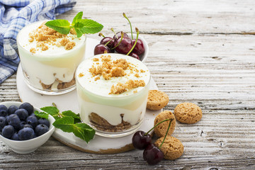 Healthy summer dessert of berry yogurt almond cookies portioned in glass cups on a light wooden background with ripe blueberries and juicy cherries. Selective focus. the concept of fitness nutrition